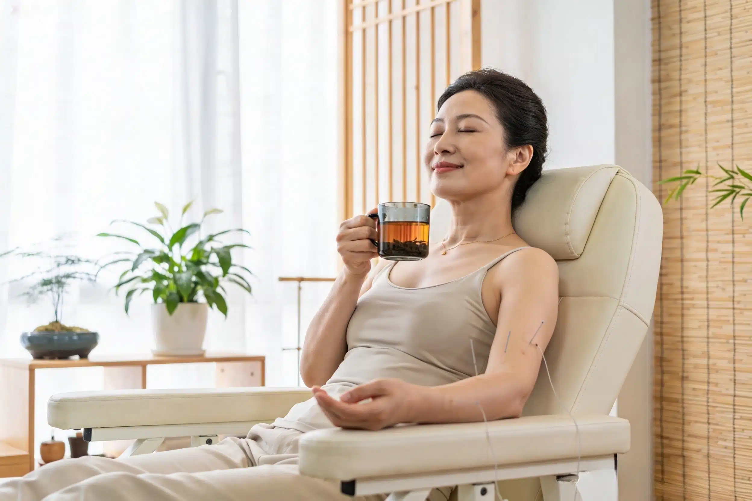 Woman sitting calmly in an acupuncture clinic, holding a cup of tea, feeling relaxed and stress‑free, acupuncture for anxiety relief Mississauga